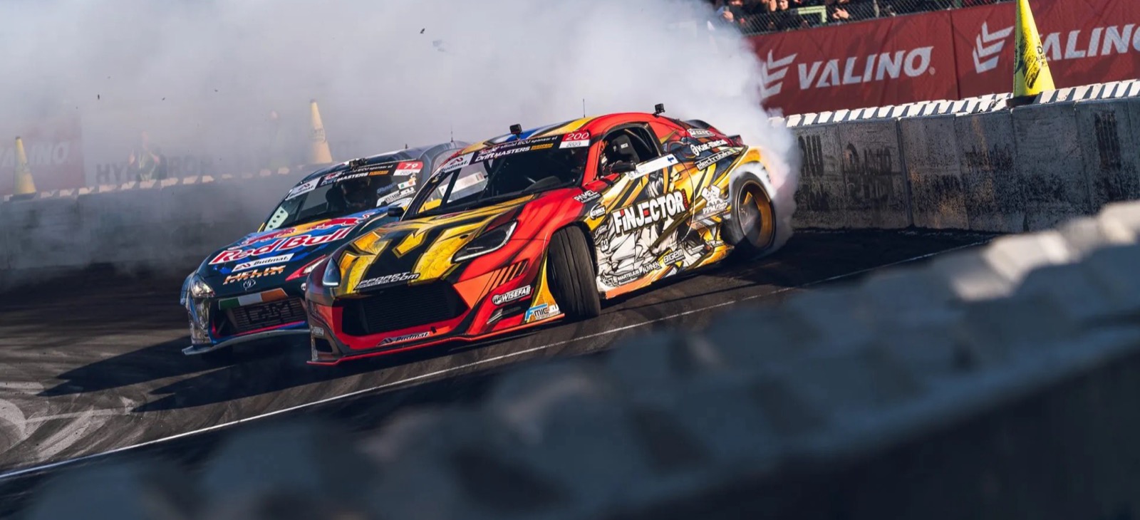 Two drift cars in a tandem battle behind a tire wall at Drift Masters